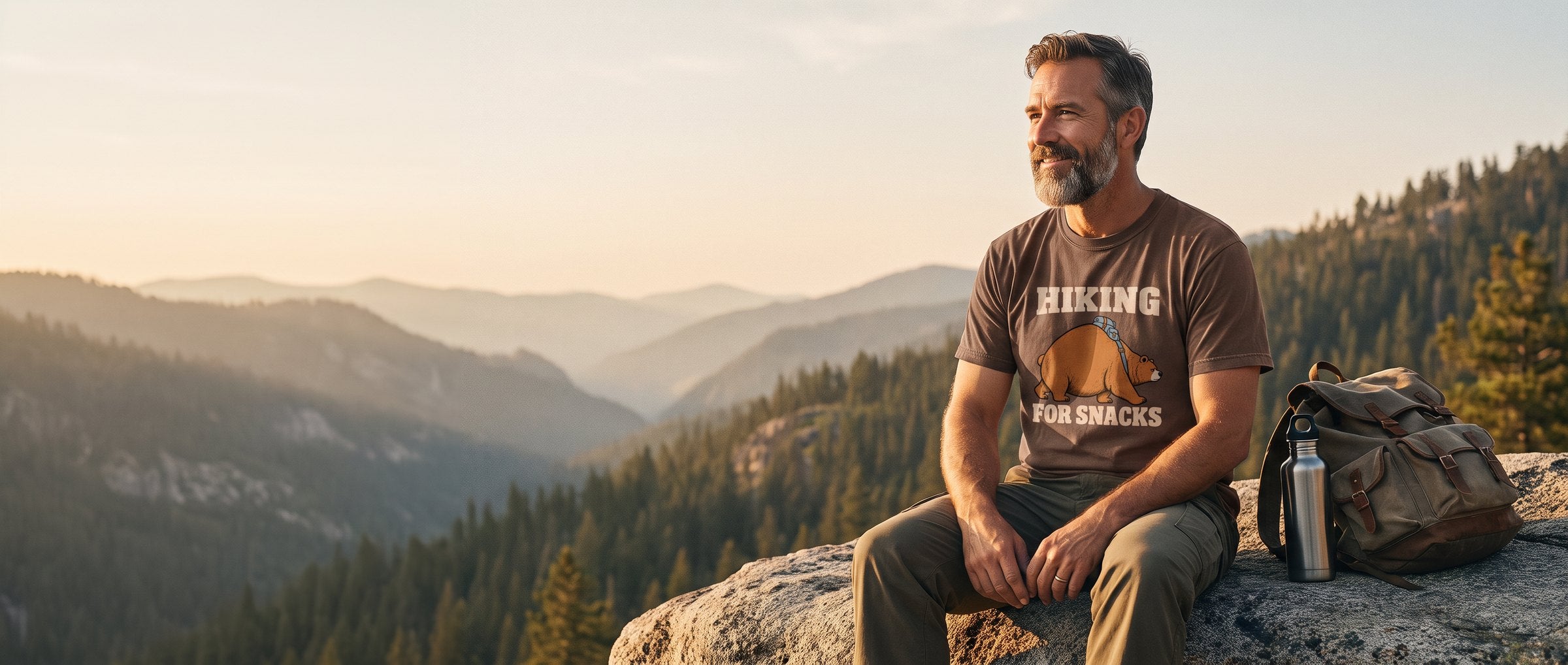 Bearded hiker resting on a granite ledge above a forested valley at golden hour, wearing the Hiking for Snacks tee in Espresso